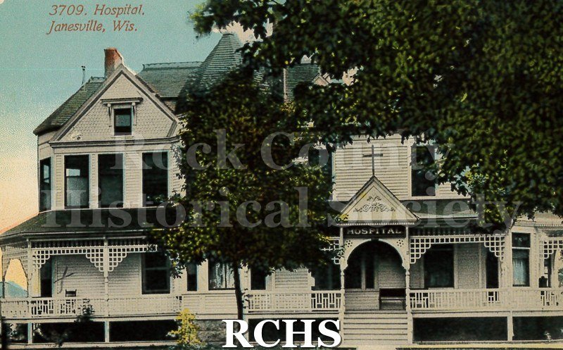 Postcard. Colorized image of the exterior of the hospital in Janesville. Postcard has a message written on the back in pencil, but no postmark.