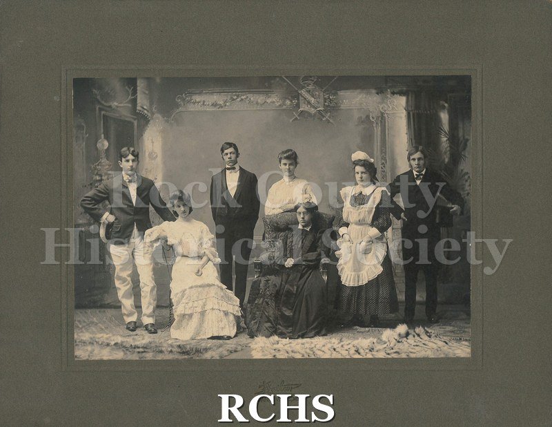 Black and white photograph of the cast of a Janesville High School play in 1904. Cora Soverhill Atwood plays the old woman who is seating down.