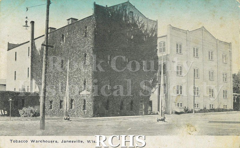Postcard. Tinted image of the exterior of the tobacco warehouses in Janesville.