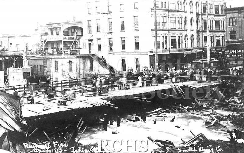 Postcard. Black and white photograph of the aftermath of a fire in downtown Janesville near the Milwaukee Street bridge in April 1913.