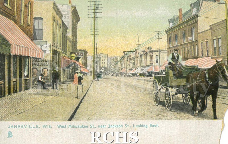 Postcard. Tinted image of West Milwaukee Street near Jackson Street in Janesville. Addressed to Clara Brigham of Hebron, Illinois. Postmarked 17 November 1908.