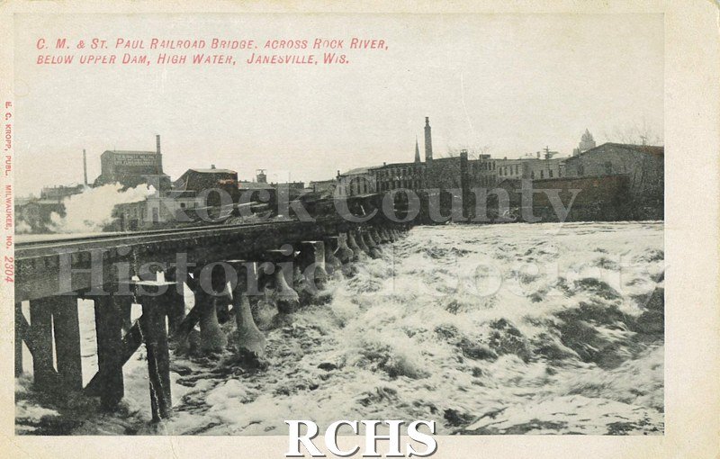 Post card with Black and white photograph of the C. M. & St. Paul Railroad bridge across the Rock River during high water on the front.