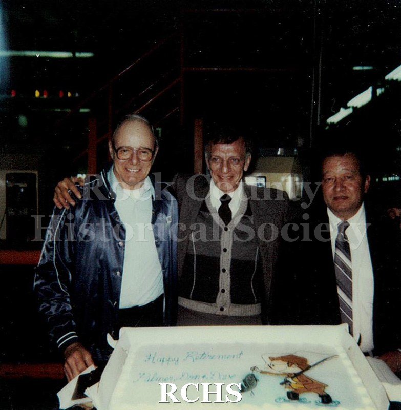 Historic image of Color Polaroid snapshot Palmer Larson and two others posed in front of a large cake at their combined retirement party from the Janesville GM.