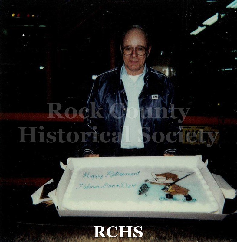 Historic image of Color Polaroid snapshot of Palmer Larson posing in front of a large cake at his retirement party from the Janesville GM plant.
