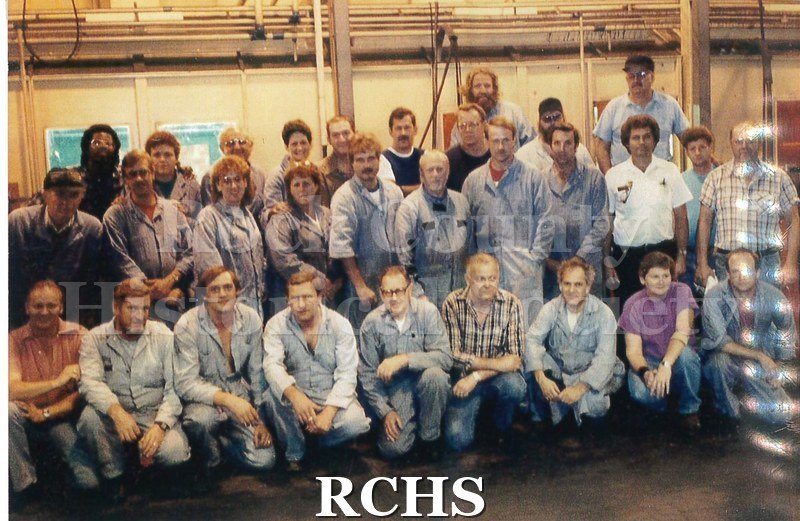 Color photo with flash of a GM employee, Chris Myers. He has short grey hair and a mustache, and is wearing a white polo shirt and dark pants.
