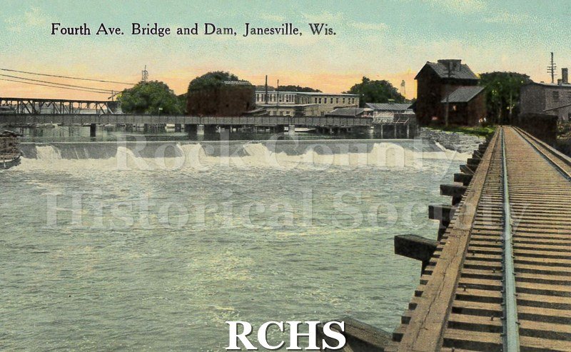 Postcard. Tinted image of the Fourth Avenue Bridge and dam in Janesville. Image is from the vantage point of the nearby railroad tracks.