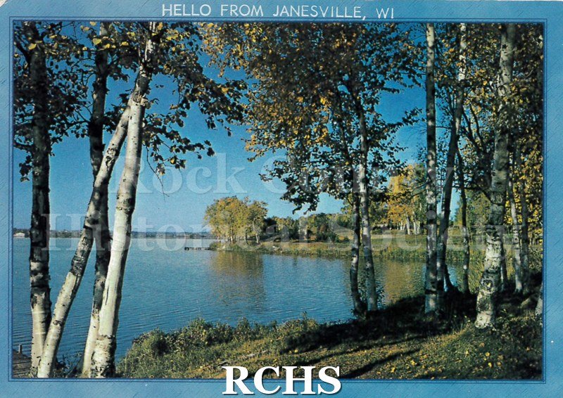 Postcard. Colored photograph of the Rock River's shoreline. Sunny day. To the far left you can make out the corner of a pier.