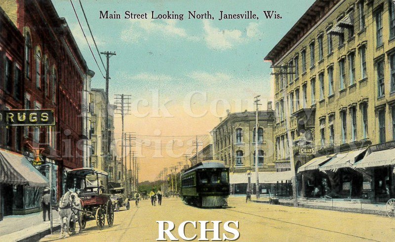 Postcard. Tinted image of Main Street in Janesville. Addressed to Emma Schless of Watertown, Wisconsin. Postmarked 2 November 1915.