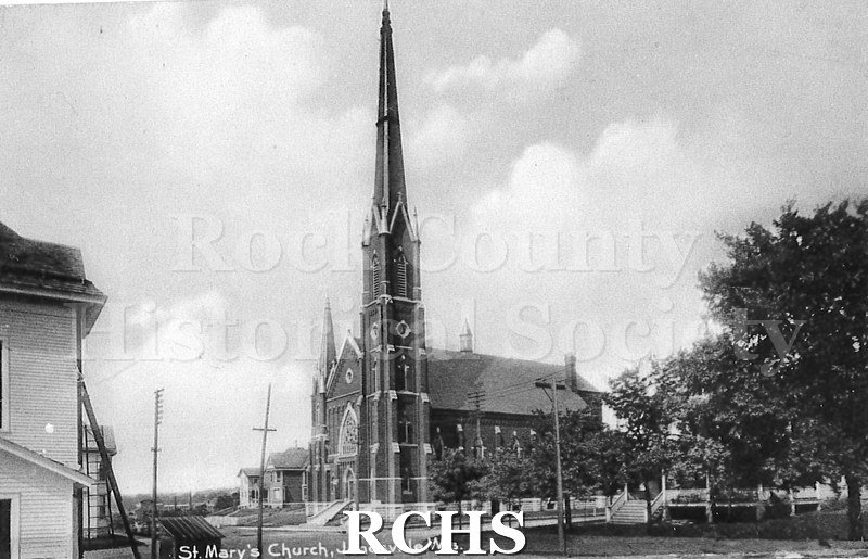 Postcard. Black and white photograph of the exterior of St. Mary's Church in Janesville and portions of the houses surrounding it.