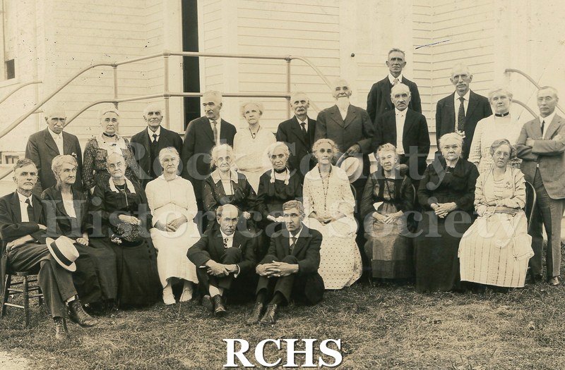 Black and white photograph of several people standing and sitting in front of Rock Prairie United Presbyterian Church.