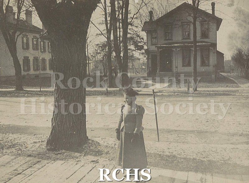 Black and white photograph of the houses of Mr. & Mrs. J. R. Botsworth, Janesville, WI, and Mr. & Mrs. Art Jackson. Shows a young woman standing near a tree.