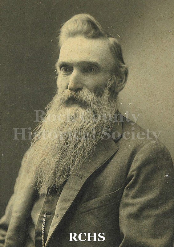 Black and white photograph of Ole Evenson wearing a dark suit jacket and having a long beard and mustache.