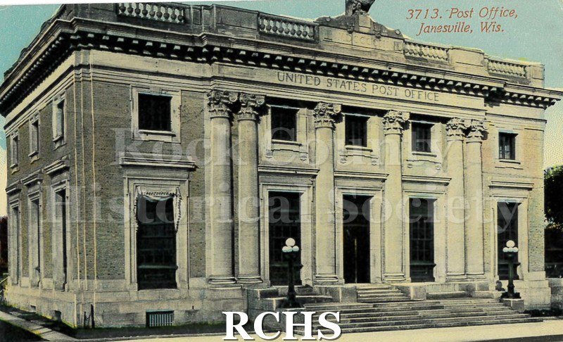 Postcard. Tinted image of the exterior of the post office in Janesville. Addressed to Jennie Buck in Janesville. Postmarked December 1914.