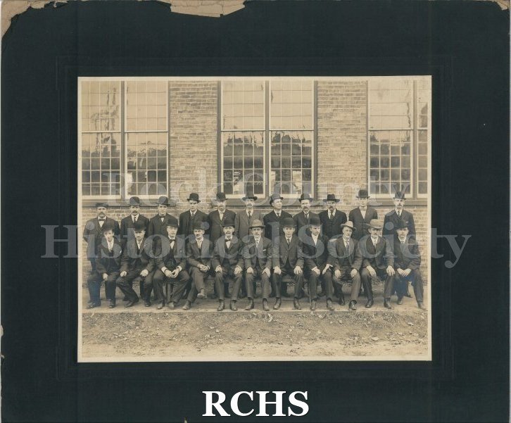Black and white photograph of Janesville Machine Company workers posed for a photo outside of a building. 22 men in two lines of 11.
