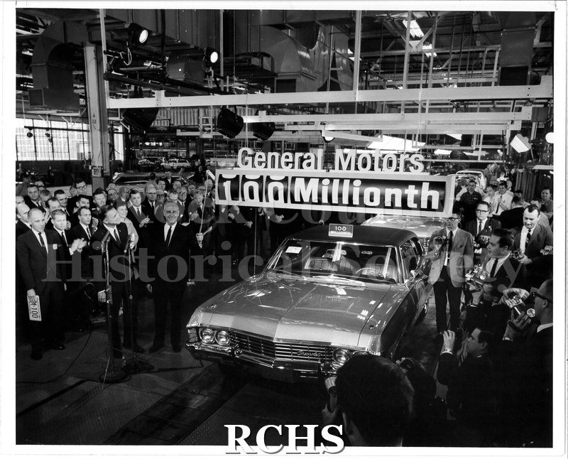 Black and white photograph of the 100 millionth GM car coming off the line. General Motors president James Roche and Wisconsin Lt. Gov.