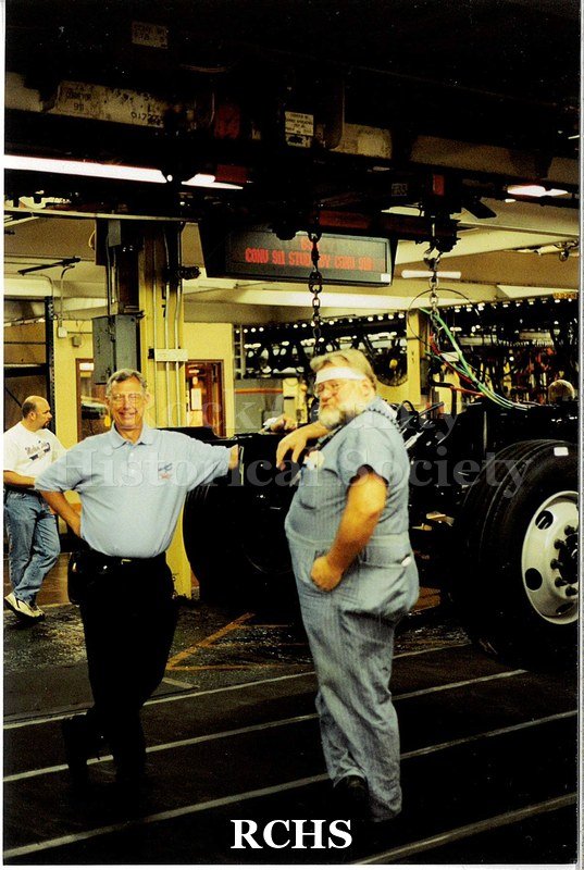Color photo of the Janesville GM plant assembly line for medium-duty trucks. Two men pose for a photo at the bed of the last medium-duty truck made in Janesville.
