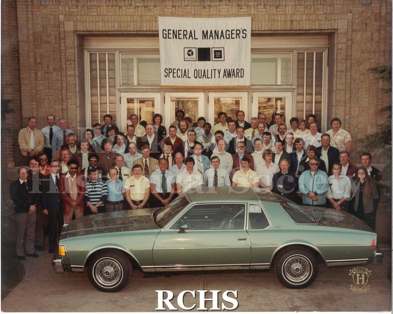 Digital color photo of GMAD supervisiors from the Janesville GM plant posing outside of the building, behind one of the cars from the plant - a 1979 Impala.