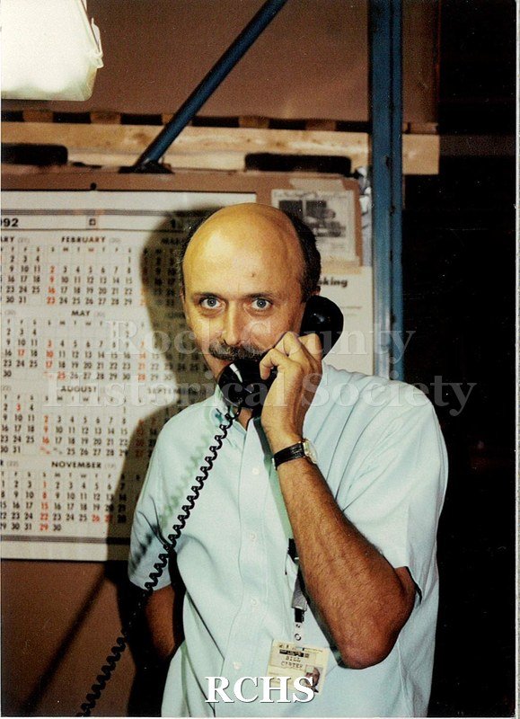 Color photo with flash of a man, Bill Carter, talking on the phone in a building. He's looking into the camera.
