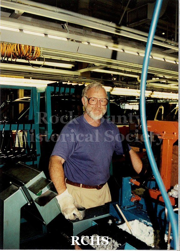 Color photo with flash of an older man, Gene Arner, at work in Janesville General Motors.