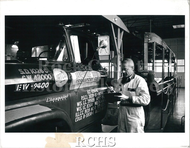 Black and white photograph of a JATCO shop worker filling out a checklist for a transport truck.
