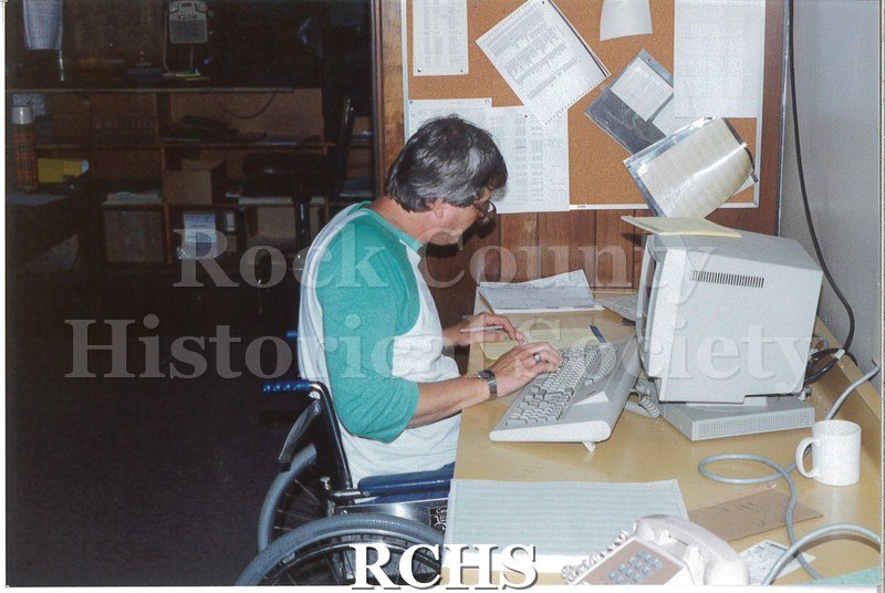 Color photo of the damage to the Janesville Terminal from the 1991 tornado. A man in a wheelchair is working at his desk.
