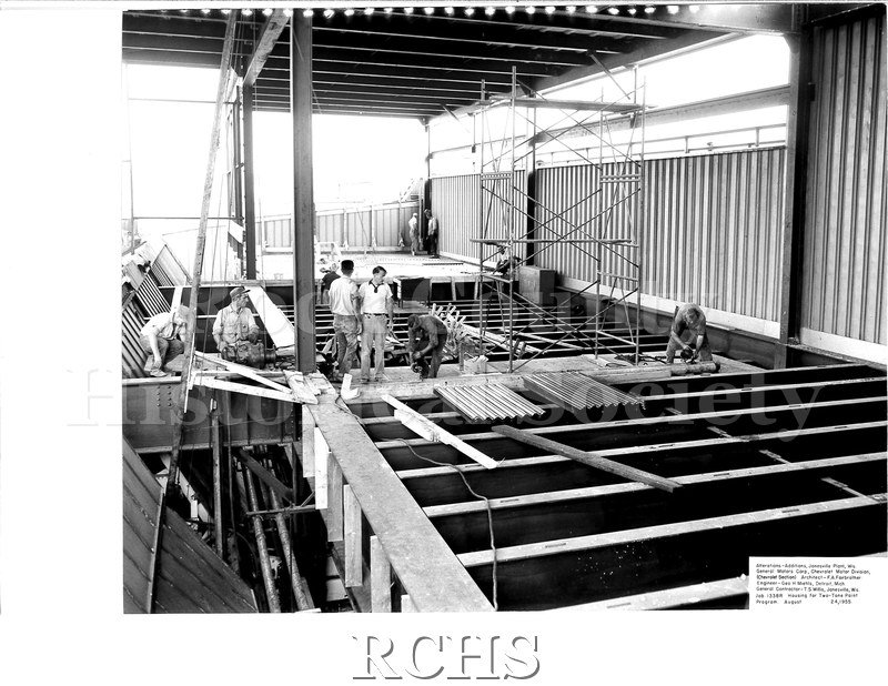 Black and white photograph of men working on the roof of a building under construction. There is scafolding on the right side.