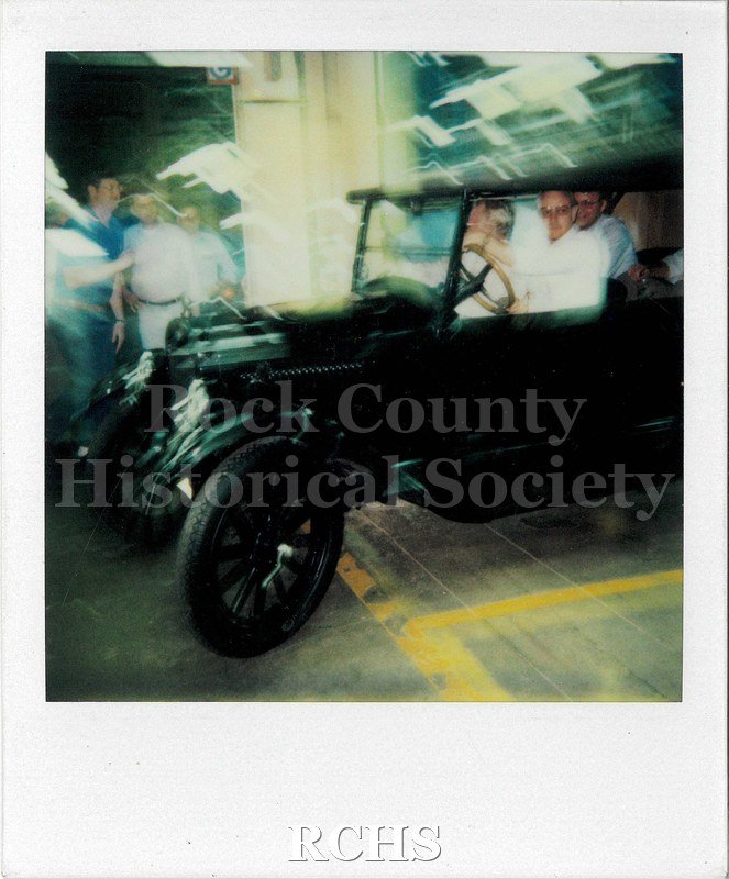 Polaroid photo of Sydney Olsen, a General Motors employee, riding in an old car. The photo is blurry from movement.