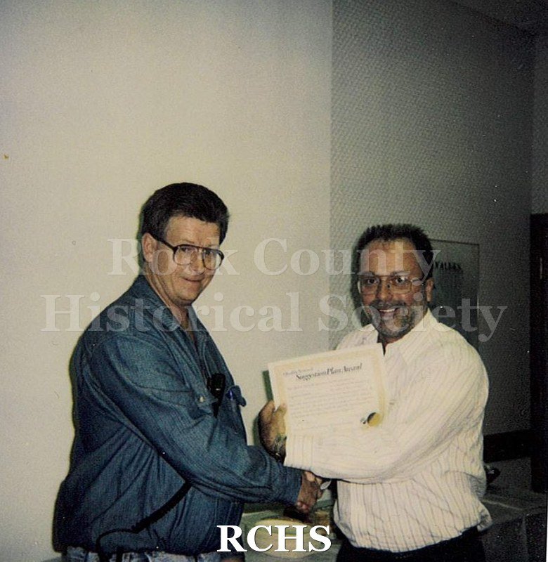 Historic image of Color Polaroid snapshot of Lyle Ackerman receiving an award certificate from an unidentified supervisor at the Janesville GM plant.
