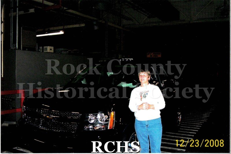Digital color photo of an employee at Janesville General Motors standing in front of the last car assembled at the plant.