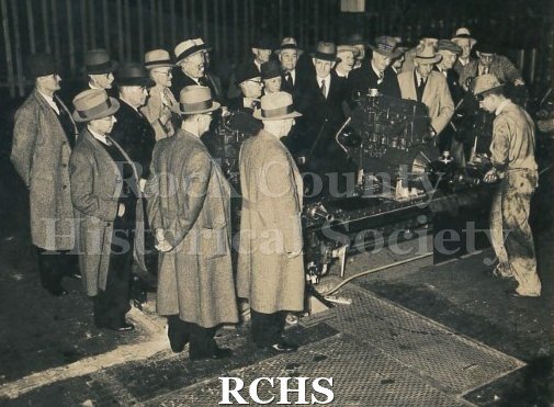 Black and white photograph of a group of gentlemen inspecting machinery at the Baltimore Chevrolet assembly plant. Thomas Butters is included in the group.
