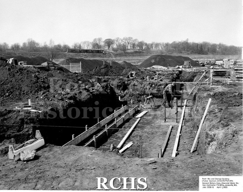 Black and white photograph of the footings being outlined at the construction site. There is a worker on the right and a hole on the left.
