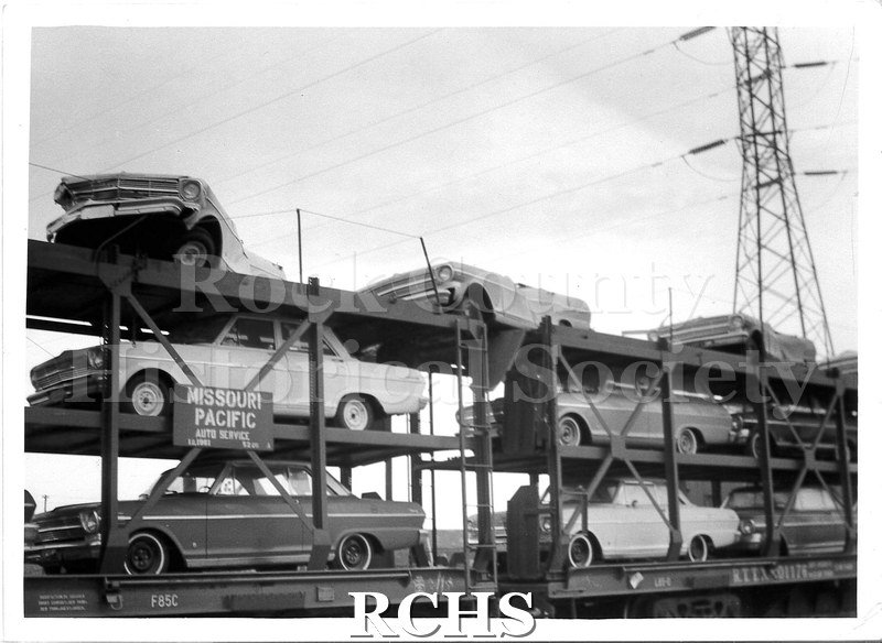Black and white photograph of vehicles produced at the Janesville GM plant loaded onto a Missouri Pacific train car for transport.
