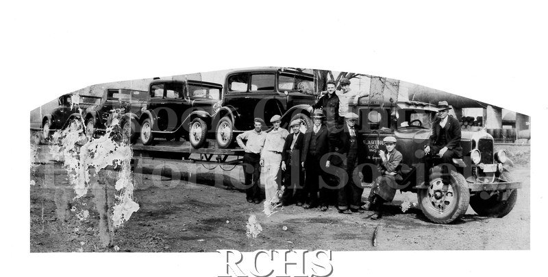 Black and white photograph of several W.R. Arthur employees standing by a trailer loaded with four Chevrolets.