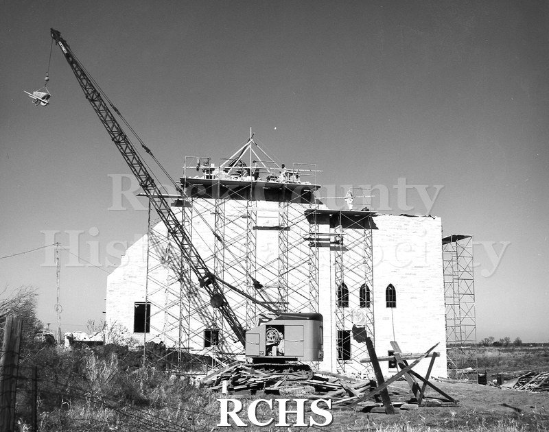 Black and white photograph of scaffolding on the front of First Lutheran Church. There is a crane with a load in front of the building.