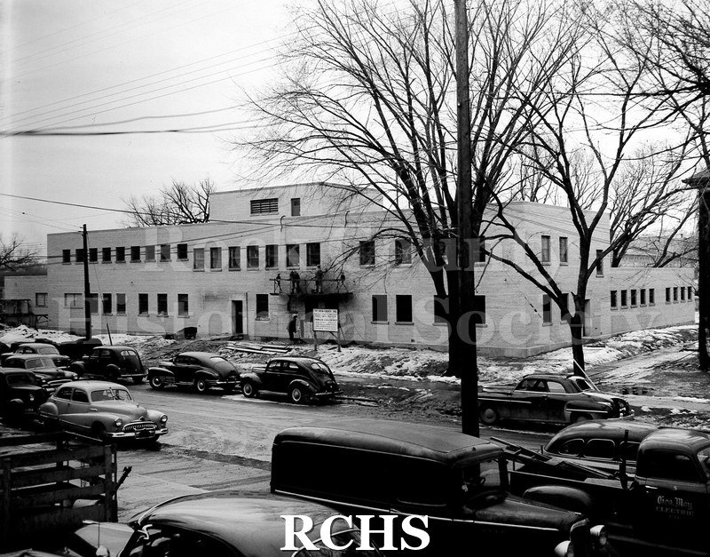 Black and white photograph of Rock County Jail shown as a building almost complete. There are men on a scaffold over the first floor.