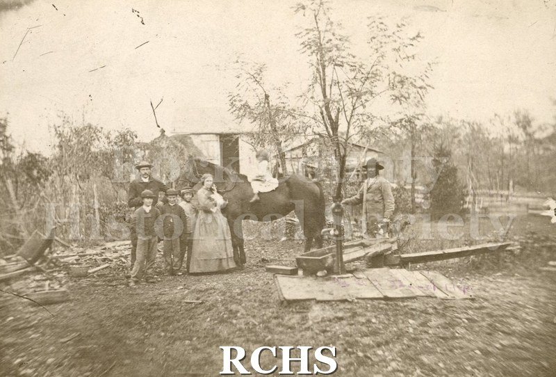Black and white photograph of Kellogg Home. Shows one woman, two men, three boys and one girl seated on back of horse. Woman holding something - baby?