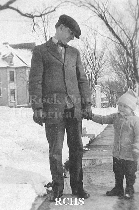 Black and white photograph of Charles N. Tallman as child, dressed in coat, hat and mittens standing with his hand in his father's Charles.