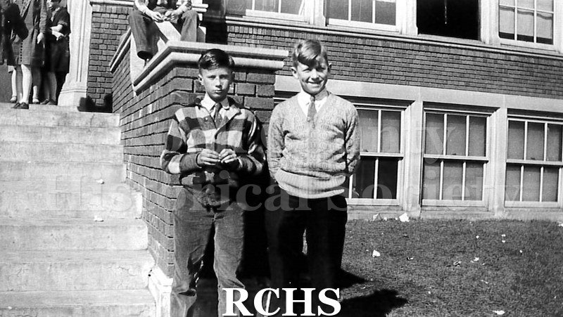 Black and white photograph of Charles N. Tallman with friend. Shows two boys dressed in shirt, tie and pants standing in front of brick building with steps and.