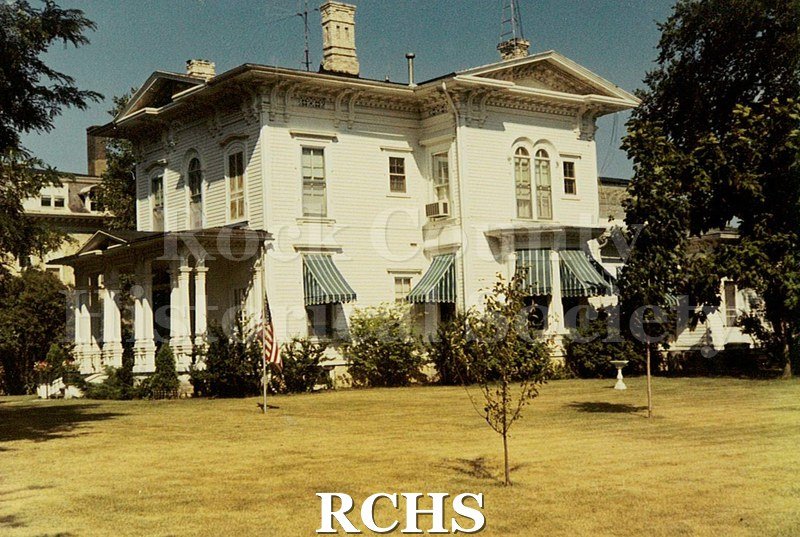 Colored photograph of an unidentified two story house on St. Lawrence Ave. Shows a pillared porch in the left; awnings on the windows; and a birdbath on the lawn.