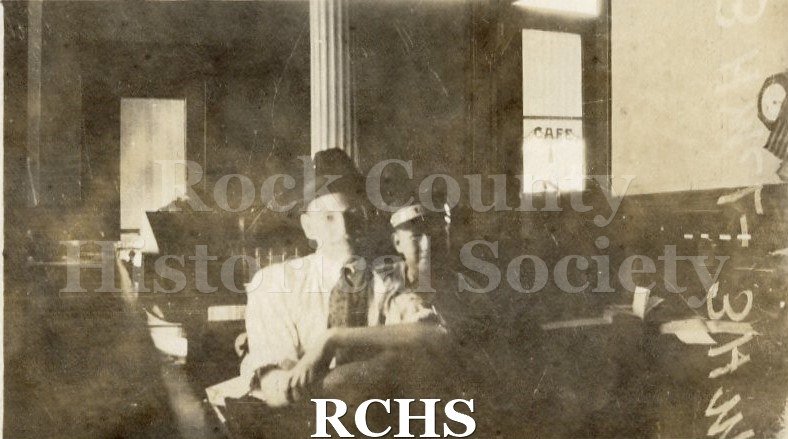 Black and white photograph of a man and a young telegraph delivery boy seated at desks at the postal telegraph office in Janesville.