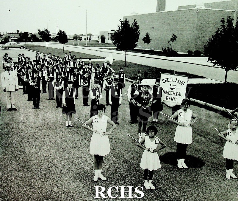 Black and white photograph of Frank Daniels marching with the Cecilians Parochial Band. The band is lined up outside of Craig High School.