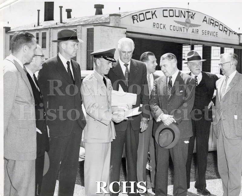 Black and white photograph of dignitaries awaiting the return of surviving members of the "Janesville Tanks" at the Rock County Airport.
