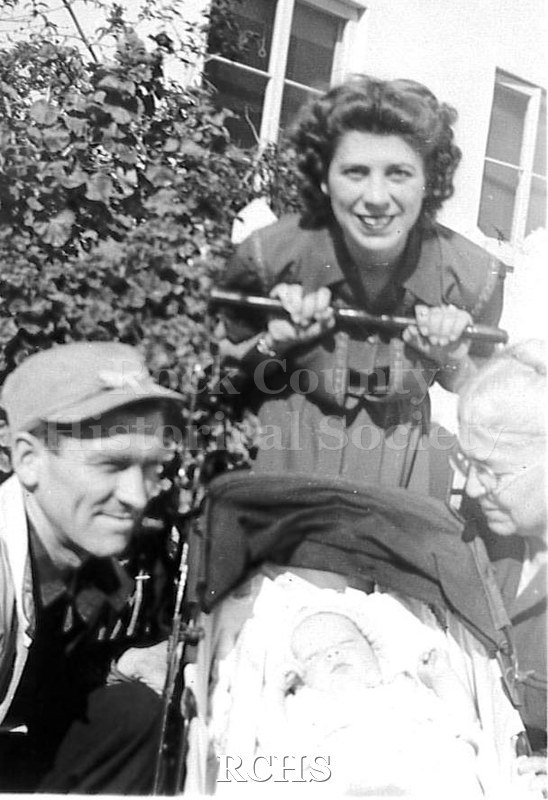 Black and white photograph of Charles N. Tallman, the kneeling man with cap, jacket, shirt and pants squatting down next to baby carriage.