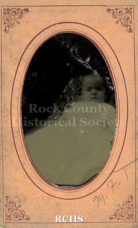 Black and white photograph of May Felton Tallman as a baby in long white dress, semi-reclining on patterned cloth.