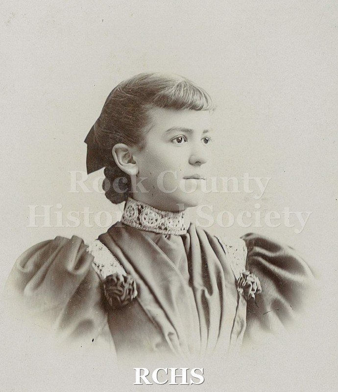 Black and white photograph of Clara May Felton Tallman in 3/4 profile. Dark hair with short curled bangs, pulled back and appears in braid with bow at back of head.