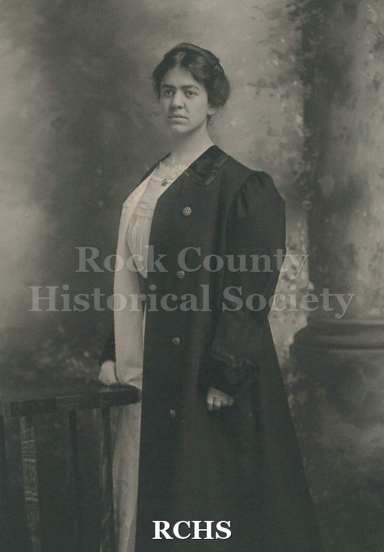 Black and white photograph of May Felton in 3/4 profile. Dressed in light colored dress with round neckline, puff sleeve to just below elbow length.