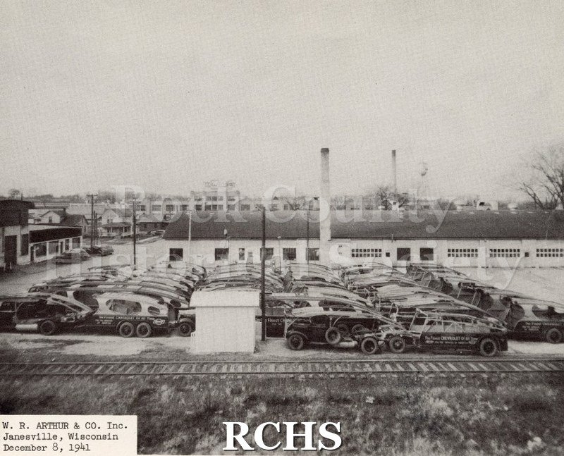 Black and white photograph of W. R. Arthur and Company Inc. loading lot building. Features several cars in differing states of completion in front of the building.