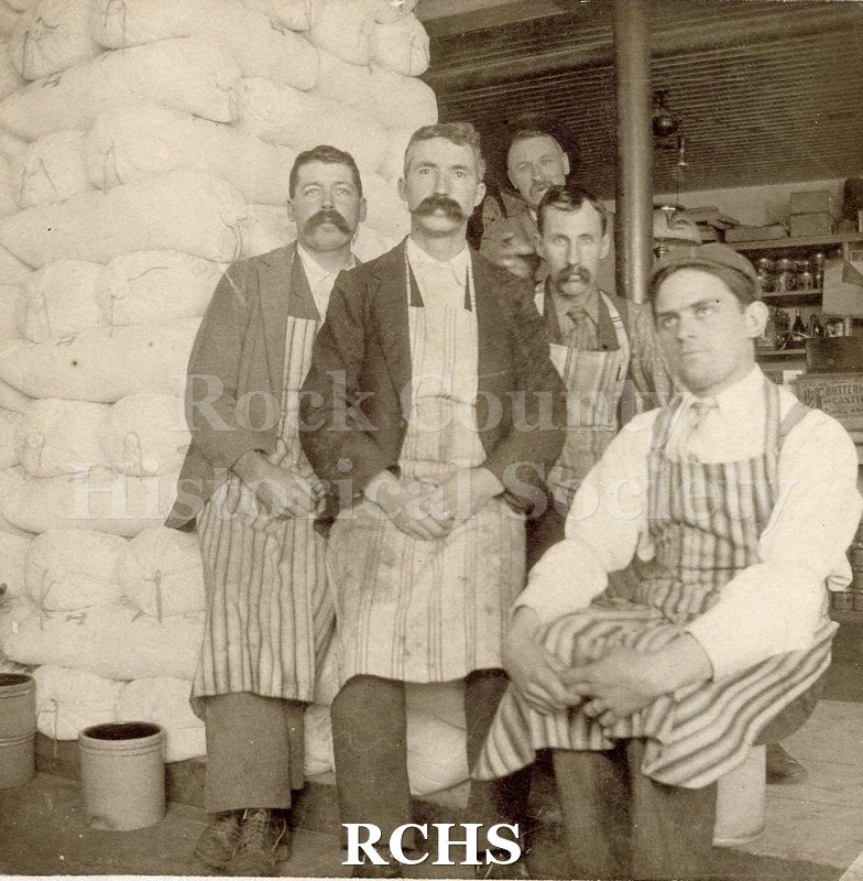 Black and white photograph of The Grange Store. Five men are sitting and standing in front of a store.