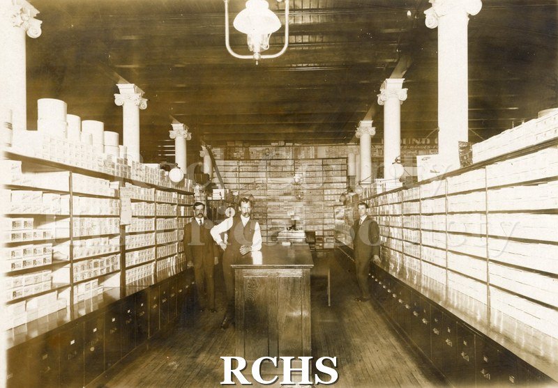 Black and white photograph of The Grange Store. Shows the inside of a shoe storage room. There are boxes of shoes on all three sides.