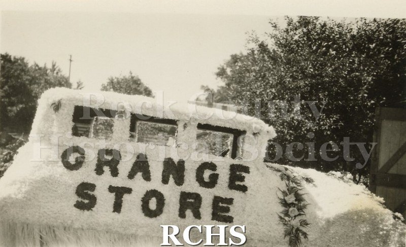 Black and white photograph of a1928 Buick. Shows a car decorated with white tissue. The words: "Grange Store" are shown in black.